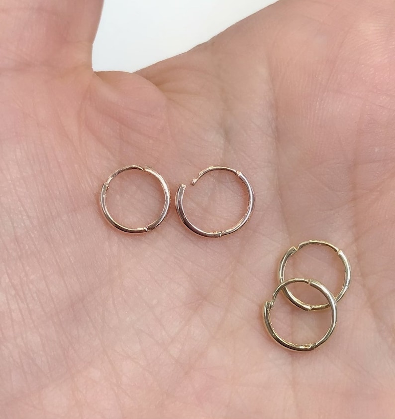 May include: Three pairs of gold hoop earrings. The earrings are different sizes. The earrings are on a hand.
