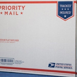 May include: A white Priority Mail flat rate box with red and blue text and accents. The box features the text "PRIORITY MAIL" and "TRACKED INSURED". The United States Postal Service logo is visible on the lower right corner.