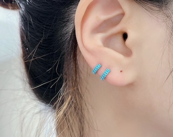 May include: A pair of small hoop earrings with turquoise stones. The earrings are made of silver and have a simple, elegant design.