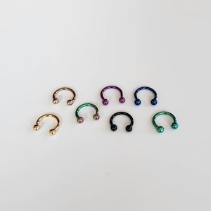 Pode incluir: Um conjunto de sete anéis em forma de ferradura com pontas de bola. Os anéis são feitos de metal e vêm em uma variedade de cores, incluindo ouro, prata, preto, azul, verde e roxo.