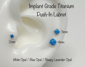 May include: Three titanium push-in labrets with opal stones in different sizes: 2mm, 3mm, and 4mm. The stones are blue, white, and sleepy lavender.