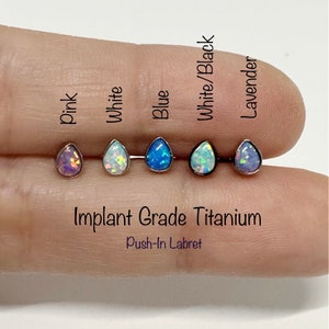 Può includere: Cinque labrets a pressione in titanio con pietre di opale in diversi colori: rosa, bianco, blu, bianco/nero e lavanda. Titanio di grado implantabile. Labret a pressione.