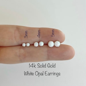 May include: Three pairs of white opal earrings in 14k solid gold, shown on a finger. The earrings are 3mm, 4mm, and 5mm in size.