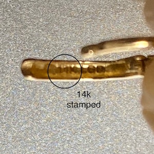 May include: Close-up of a gold-colored metal band with the marking "14k stamped" on the inside.