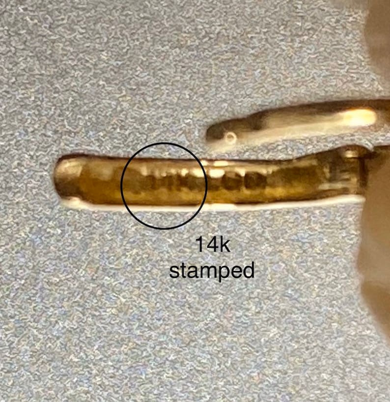 May include: Close-up of a gold-colored metal band with the marking "14k stamped" on the inside.