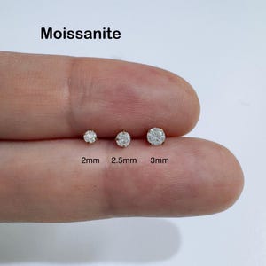 May include: Three moissanite stud earrings in 2mm, 2.5mm, and 3mm sizes. The earrings are round-cut with a clear, sparkling appearance. The text "Moissanite" is above the earrings.