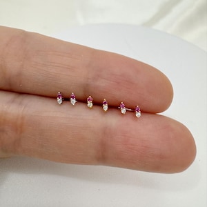 May include: Five pairs of small, dainty earrings with a single pink and white gemstone on each earring. The earrings are displayed on a finger.