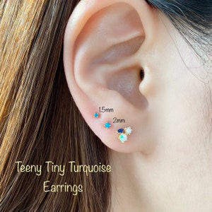 May include: Close-up of a person's ear with three small turquoise, blue, and white gemstone earrings. The earrings are 1.5mm and 2mm in size. The caption reads "Teeny Tiny Turquoise Earrings".