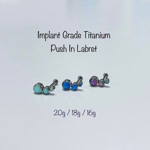 May include: Three titanium labrets with opal stones. The labrets are available in 20g, 18g, and 16g. The opal stones are blue, light blue, and pink.