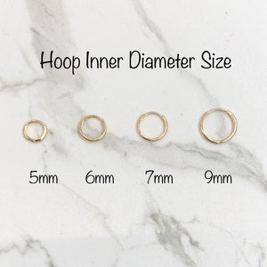May include: Four gold hoop earrings in different sizes, 5mm, 6mm, 7mm, and 9mm. The earrings are displayed on a white marble surface.