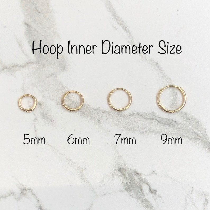 May include: Four gold hoop earrings in different sizes, 5mm, 6mm, 7mm, and 9mm. The earrings are displayed on a white marble surface.