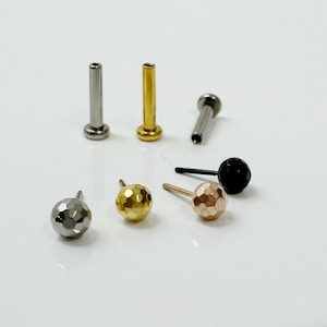 May include: A set of six body jewelry pieces, including three different colored ball ends and three different colored posts. The ball ends are silver, gold, and rose gold, and the posts are silver, gold, and black.