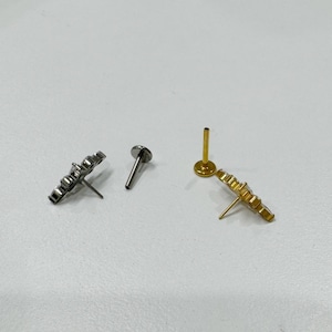 May include: Two stud earrings, one silver and one gold, each with a flower-like design. The silver earring has a flat back and a post. The gold earring has a flat back and a post. The earrings are on a white surface.