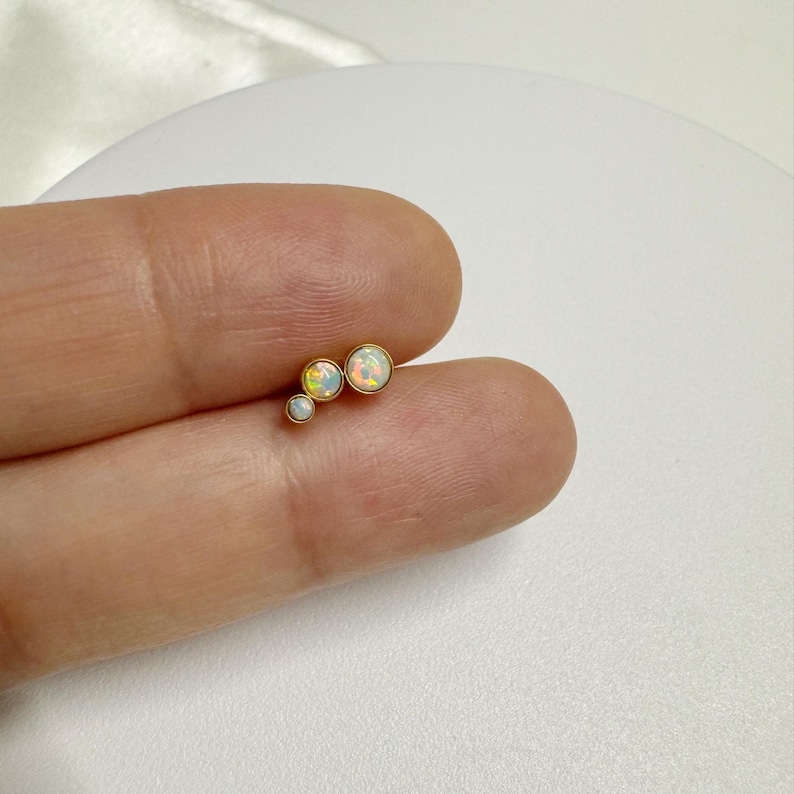 May include: Three gold-toned opal earrings in a graduated size, arranged in a curved line.