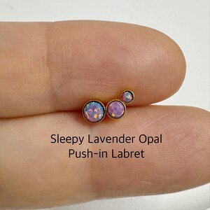 May include: Three gold push-in labrets with lavender opal stones. The stones are different sizes and are arranged in a cluster.