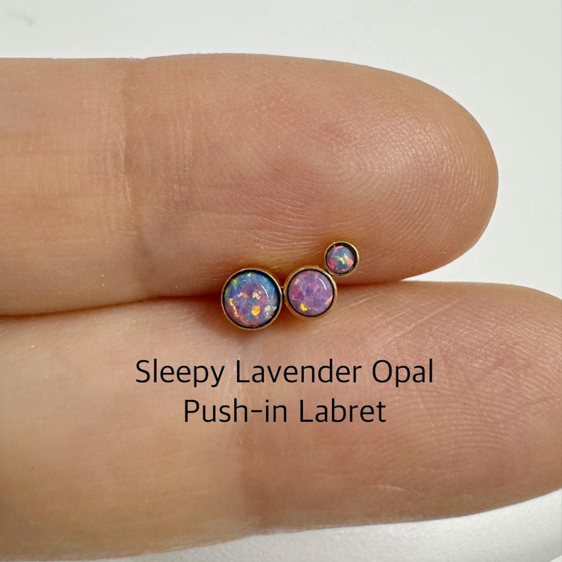 May include: Three gold push-in labrets with lavender opal stones. The stones are different sizes and are arranged in a cluster.