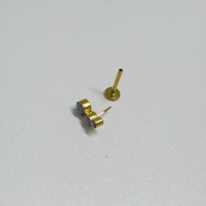 May include: A gold-toned body jewelry piece with three opal-like stones. The jewelry is separated into two parts: a post with a small ball on the end and a cluster of three stones.