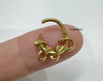 May include: A gold-colored hoop earring with a knot design. The earring is made of a shiny, metallic material and features a hinged closure. The earring is shown on a finger against a white background.