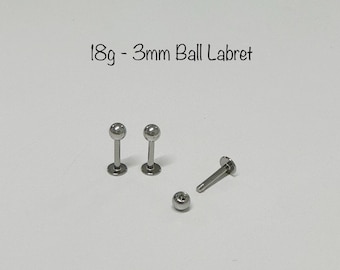 Può includere: Tre labrets in argento da 18 gauge con sfere da 3 mm. Un labret è smontato, mostrando l'asta e la sfera separatamente.