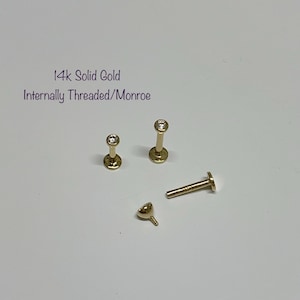 May include: Four 14k solid gold internally threaded Monroe piercing studs with clear gemstones. The studs are arranged on a white surface.