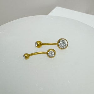 May include: Two gold belly button rings with clear crystal stones.