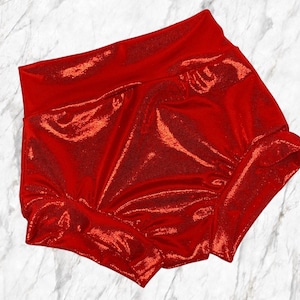May include: Red shimmery shorts with a wide elastic waistband. The shorts are made of a soft, stretchy fabric and have a ruffled hem.