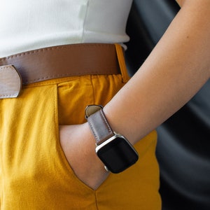 May include: A person wearing a white shirt, brown belt, and yellow trousers with a brown leather wristwatch with a black face.