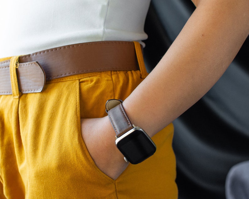 May include: A person wearing a white shirt, brown belt, and yellow trousers with a brown leather wristwatch with a black face.