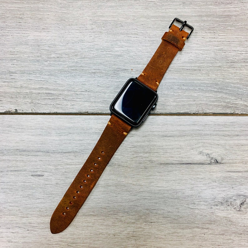 Peut inclure: Un bracelet de montre Apple en cuir marron avec un cadran noir.