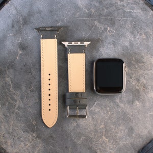 K&ouml;nnte beinhalten: Zwei schwarze Lederarmb&auml;nder mit silberner Hardware und einem schwarzen Apple Watch-Zifferblatt.