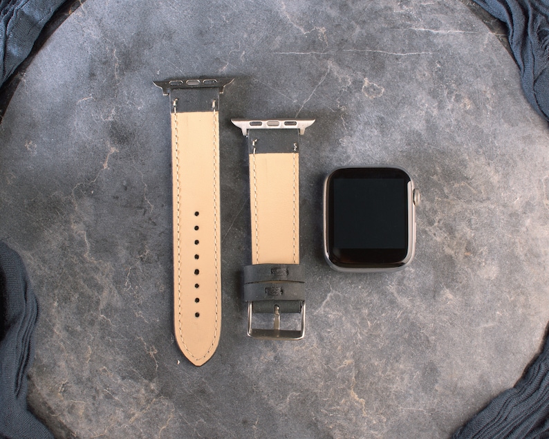 K&ouml;nnte beinhalten: Zwei schwarze Lederarmb&auml;nder mit silberner Hardware und einem schwarzen Apple Watch-Zifferblatt.