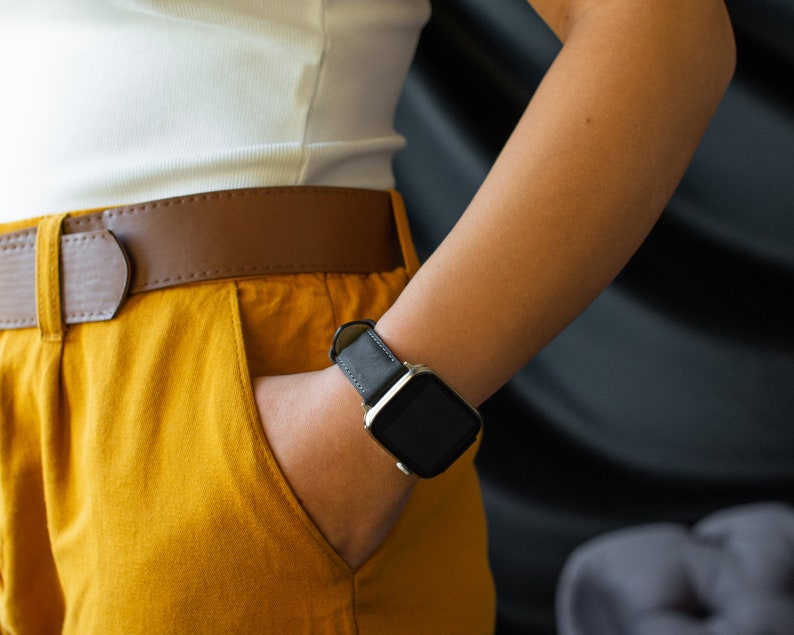 K&ouml;nnte beinhalten: Eine Person tr&auml;gt ein wei&szlig;es Tanktop und eine senfgelbe Hose mit einem braunen Lederg&uuml;rtel. Die Person tr&auml;gt eine schwarze Smartwatch mit einem silbernen Armband am linken Handgelenk.