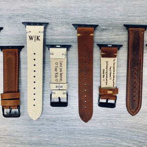 May include: Eight different leather watch bands with various engravings. The bands are brown and white and have black clasps. The engravings include initials, a heart, and a quote.