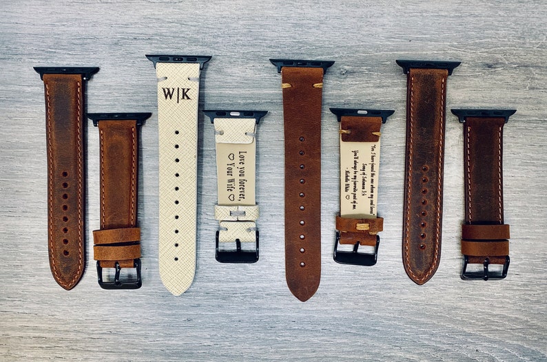 May include: Eight different leather watch bands with various engravings. The bands are brown and white and have black clasps. The engravings include initials, a heart, and a quote.