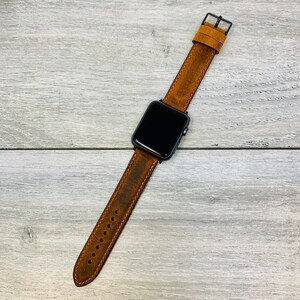 May include: A brown leather watch band with a black watch face. The band has a distressed look and is designed for an Apple Watch.