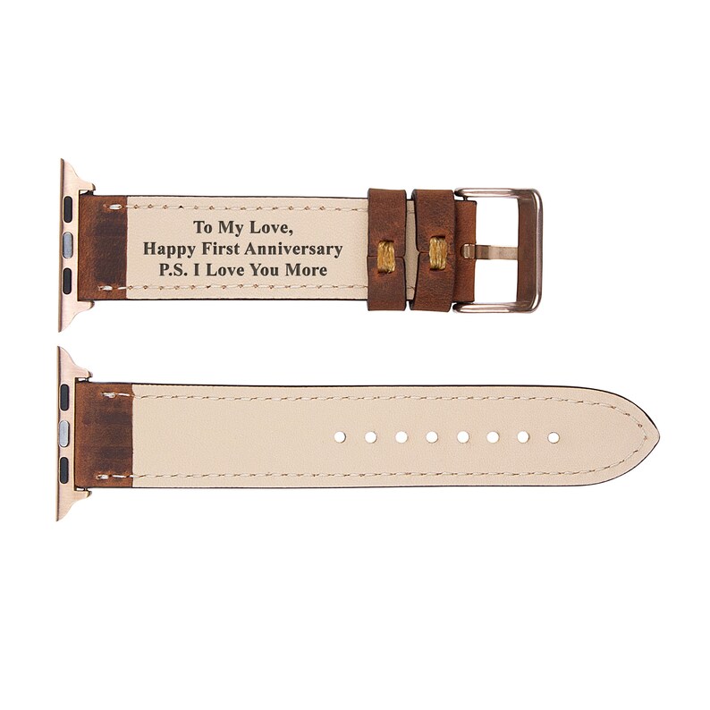 May include: Brown leather Apple Watch band with a gold buckle. The band has a personalized message that reads "To My Love, Happy First Anniversary P.S. I Love You More".