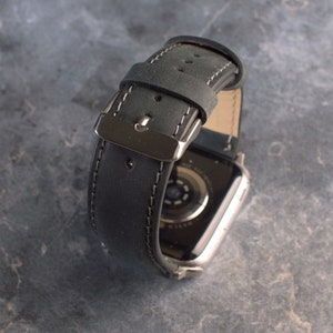 K&ouml;nnte beinhalten: Schwarzes Lederarmband mit wei&szlig;en N&auml;hten und einer silbernen Schlie&szlig;e. Das Armband ist f&uuml;r eine Smartwatch konzipiert.