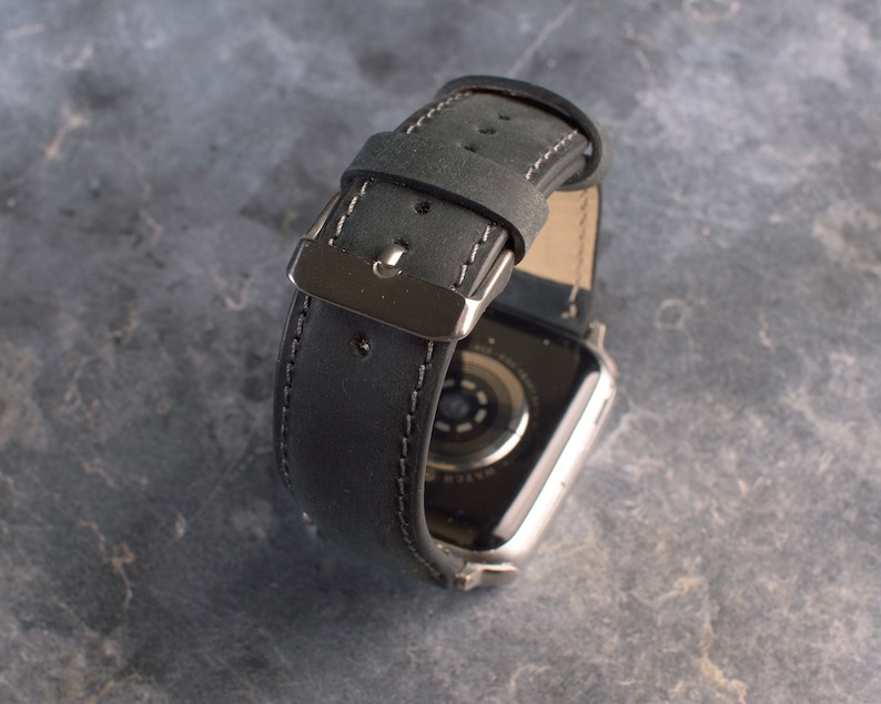 K&ouml;nnte beinhalten: Schwarzes Lederarmband mit wei&szlig;en N&auml;hten und einer silbernen Schlie&szlig;e. Das Armband ist f&uuml;r eine Smartwatch konzipiert.