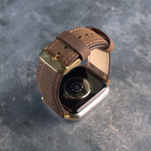 May include: A brown leather watch strap with a gold buckle. The strap is designed for a smartwatch.