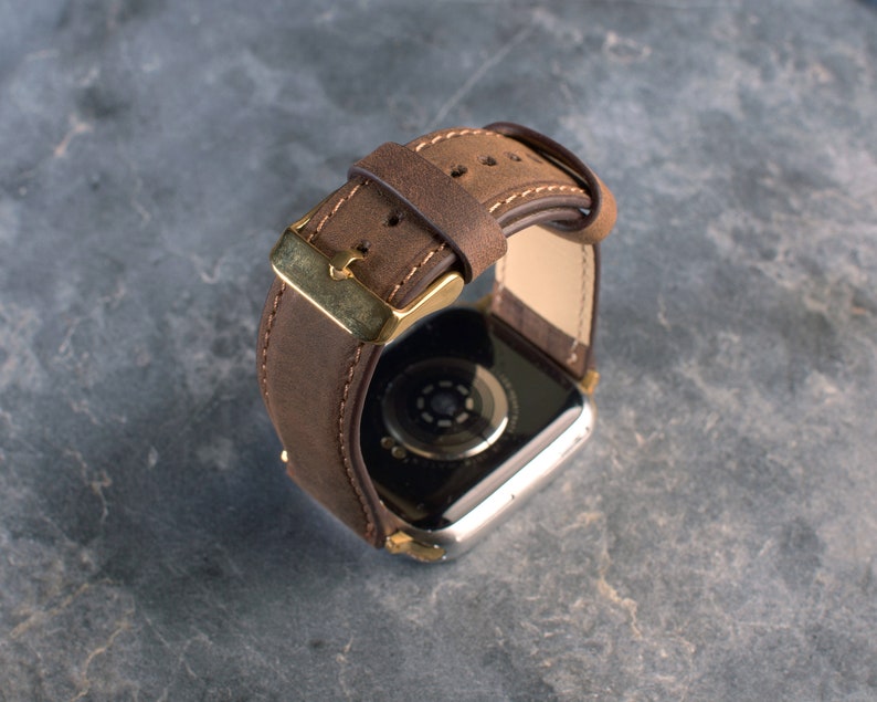 May include: A brown leather watch strap with a gold buckle. The strap is designed for a smartwatch.