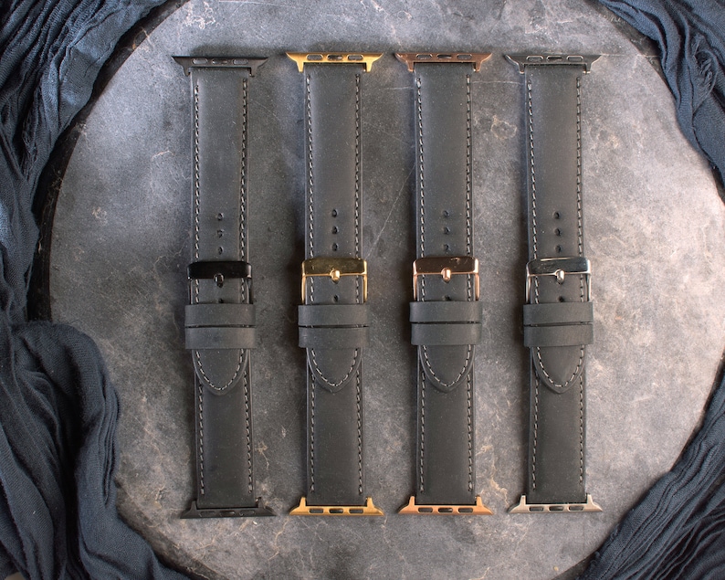 K&ouml;nnte beinhalten: Vier schwarze Lederarmb&auml;nder mit verschiedenen farbigen Verschl&uuml;ssen. Die Armb&auml;nder sind alle im gleichen Stil und haben wei&szlig;e N&auml;hte. Die Verschl&uuml;sse sind schwarz, gold, ros&eacute;gold und silber.