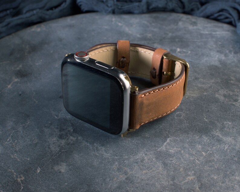 Puede incluir: Una correa de reloj de cuero marr&oacute;n con un Apple Watch plateado y negro.