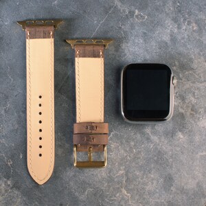 May include: Two brown leather watch straps with gold hardware and a black Apple Watch face.