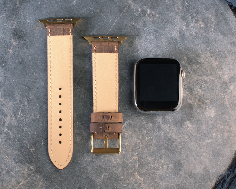 May include: Two brown leather watch straps with gold hardware and a black Apple Watch face.