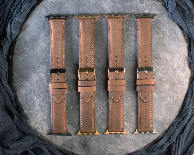 May include: Four brown leather watch straps with different coloured metal clasps. The straps are laid out on a grey surface.