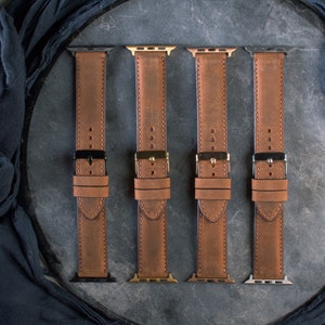 Puede incluir: Cuatro correas de reloj de cuero marr&oacute;n con cierres de diferentes colores. Las correas est&aacute;n dispuestas sobre una superficie gris.