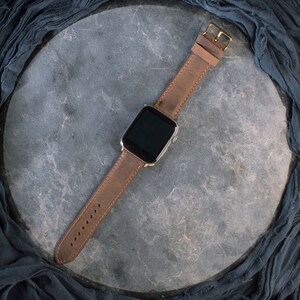 May include: A brown leather watch strap with a gold buckle and a silver smartwatch face.