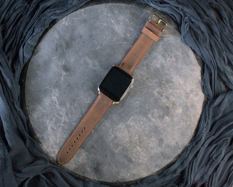 May include: A brown leather watch strap with a gold buckle and a silver smartwatch face.