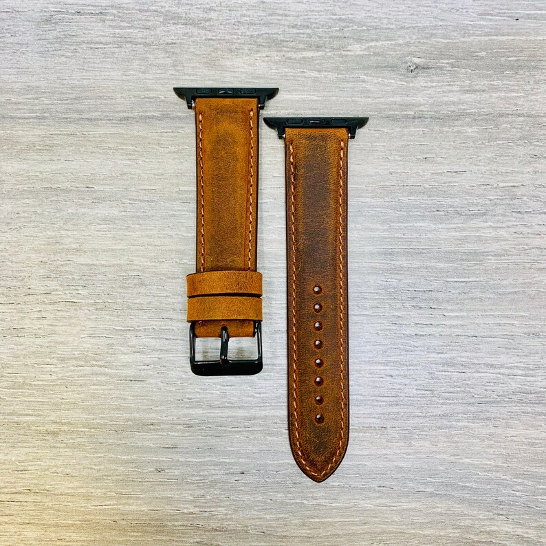 May include: Two brown leather watch bands with black metal clasps. The bands have a distressed look and are designed for Apple Watches.