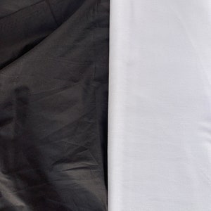 May include: A close-up of two fabric swatches, one black and one white. The black fabric is smooth and has a slight sheen, while the white fabric is textured and has a matte finish.